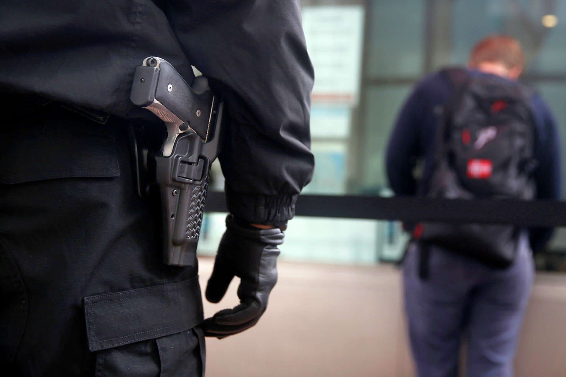 A person in black jacket holding gun near wall.