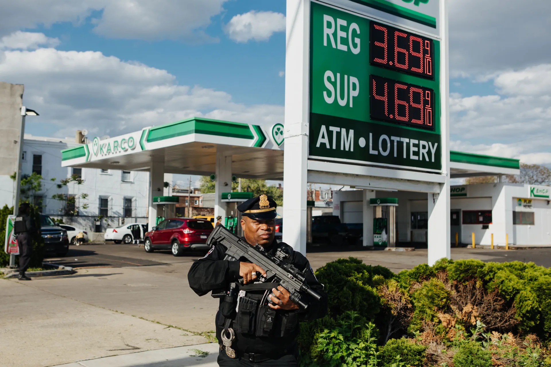 A man in uniform holding a gun near gas pumps.