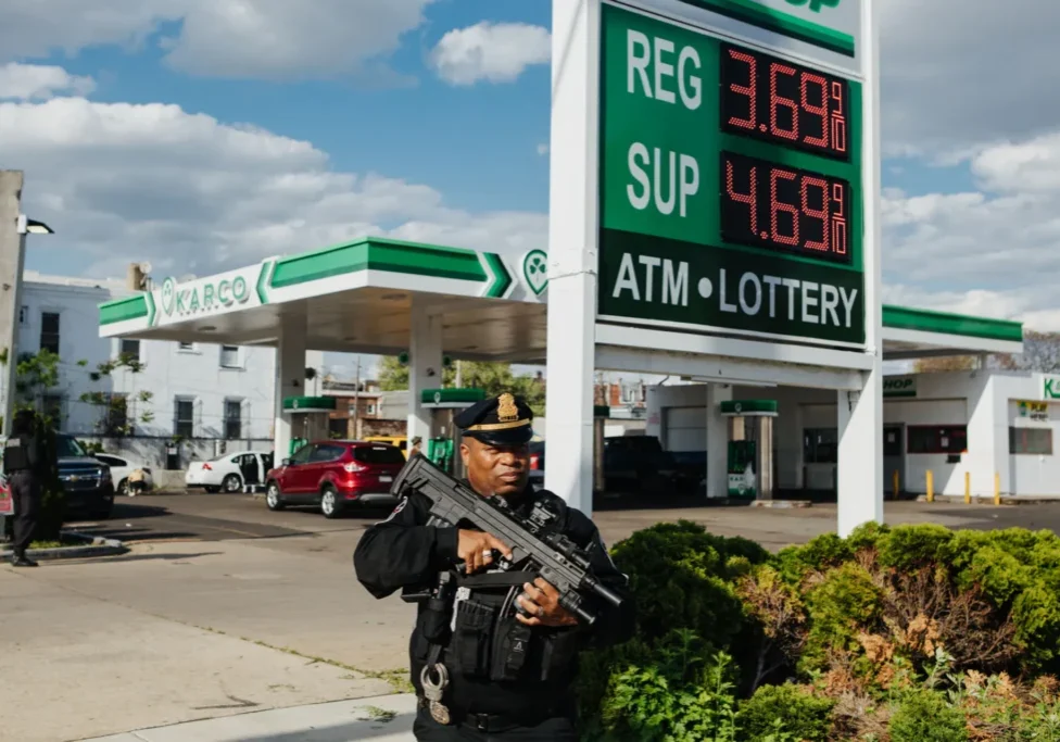 A man in uniform holding a gun near gas pumps.